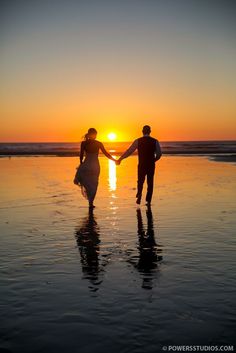 two people holding hands while walking on the beach at sunset