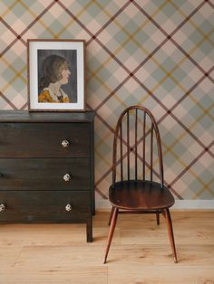 a wooden chair next to a dresser with a painting on the wall behind it and a framed portrait