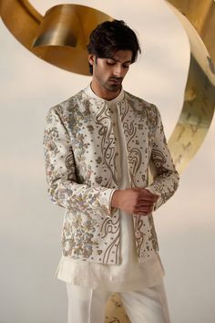 Eleven Eleven Short Jacket | Jatin Malik Introducing our renowned Short Jacket silhouette in a sophisticated dirty ivory color. This exquisite piece is hand-embroidered with colorful resham threads, gold zari, dabka, and twisted line details, creating a vibrant and intricate design. Paired with a short-length kurta featuring potli buttons and tapered trousers, this ensemble perfectly balances traditional craftsmanship with modern elegance. Ideal for making a standout impression at any special occasion, this outfit showcases our commitment to impeccable style and refined artistry. Included in purchase: Short Jacket, Kurta, Trousers Product Specification Color: Ivory Fabric: Linen Silk Occasion: Engagement, Wedding, Bridal, Reception Style: Short Jacket, Kurta, Trousers Care: Dry Clean Work: Bandhgala Kurta For Men, Indian Men Wedding Outfit Groom Attire, Nawabi Style Men, Traditional For Men, Men In Traditional, Engagement Dress For Men, Jatin Malik, Potli Button