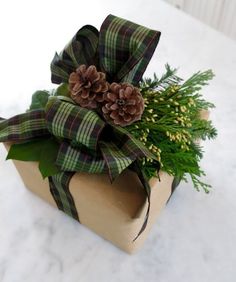 a wrapped present with pine cones and greenery sits on a marble countertop, ready to be used as a centerpiece