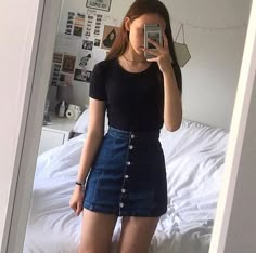 a woman taking a selfie in front of a mirror while wearing a black shirt and denim skirt