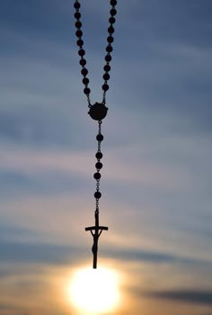 a rosary with a cross hanging from it in front of the sun at sunset or dawn