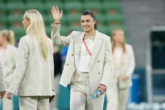 two women in business attire wave to the crowd as they stand on a soccer field