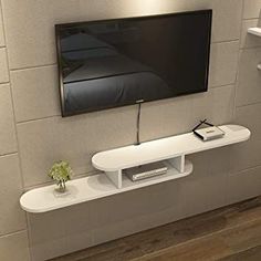 a flat screen tv mounted to the side of a wall next to a shelf with a phone on it