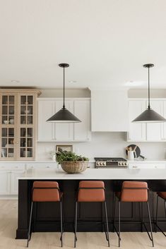 a large kitchen with white cabinets and black counter tops, three orange chairs in front of the island