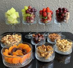 a table topped with glass bowls filled with fruit and crackers next to wine glasses