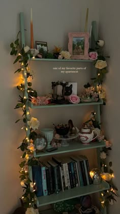 a shelf filled with lots of books and flowers next to a wall covered in lights