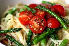 a white bowl filled with pasta, asparagus and cherry tomatoes on top of it