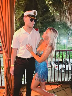 a man standing next to a woman in front of a balcony with a fence and palm trees