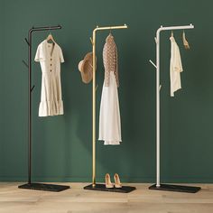 three clothing racks with hats, shoes and shirts hanging on them in front of a green wall