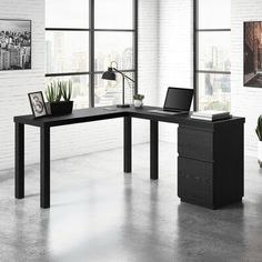 an office desk with a laptop on it in front of two windows and a potted plant