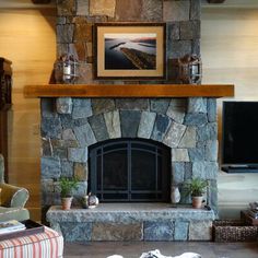 a living room with a stone fireplace and television on the wall, couches in front of it