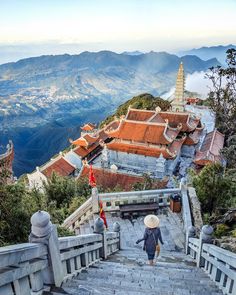 a person with a hat walking up some stairs to the top of a building on a mountain