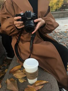 a woman sitting on the ground holding a camera and taking a photo with her coffee