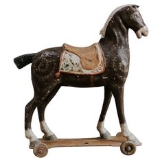 a wooden toy horse with saddle on wheels