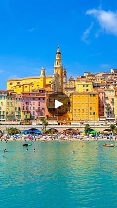 people are swimming in the water near buildings and beach umbrellas on a sunny day