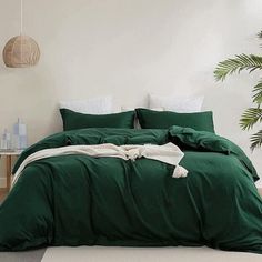 a bed with green sheets and pillows in a room next to a potted plant