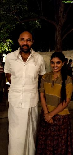 a man and woman standing next to each other in front of a tree at night