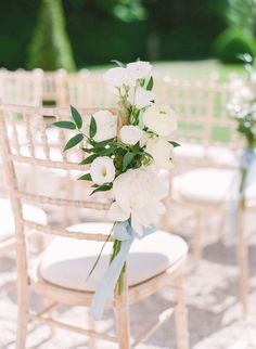 white flowers and greenery are tied to the back of chairs