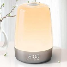 an alarm clock sitting on top of a table next to a vase with flowers in it