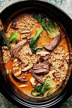 a bowl filled with noodles, meat and broccoli on top of a table