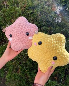 two people holding up stuffed animals in front of some bushes and trees, one is yellow and the other is pink