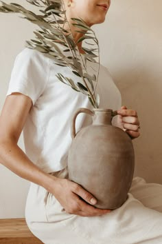 a woman holding a vase with plants growing out of it