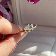 a person is holding a ring with a diamond on it in front of a flower