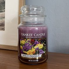 a yankee candle sitting on top of a wooden table next to a framed photo and flowers