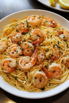 pasta with shrimp and parsley in a white bowl on a table next to lemon wedges