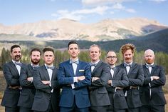 a group of men standing next to each other wearing suits and bow ties with mountains in the background