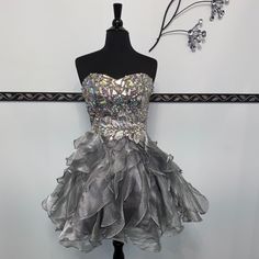 This Short Dress Features A Beautiful Jeweled Bodice, Cute Ruffle Skirt, With Side Zipper Closure. Clearance Style, As Is. Hoco Dresses Silver, Glamorous Cocktail Mini Dress With Ruffled Skirt, Glamorous Metallic Mini Dress For Prom, Cocktail Mini Dress With Ruffles And Voluminous Skirt, Mini Sequin Prom Dress With Ruffles, Glamorous Mini Corset Dress With Ruffles, Short Poofy Dresses, Unique Hoco Dresses, Halter Homecoming Dress