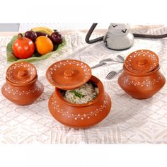 three brown pots sitting on top of a table next to a plate with fruit in it