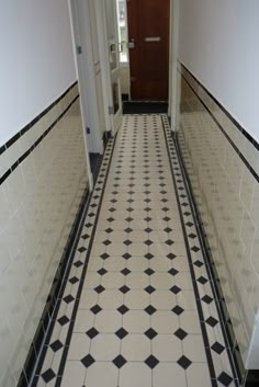 an empty hallway with black and white tiles on the floor, along with a brown door