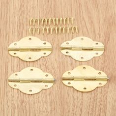 four brass plated hinges and screws on a wooden surface