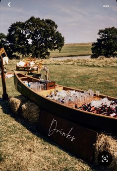 a wooden boat filled with bottles and glasses on top of dry grass next to a lake