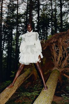 a woman standing on top of a log in the woods