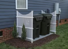 two trash cans in front of a house with a white picket fence on the side