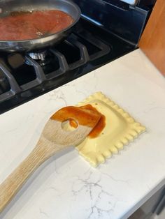 a wooden spatula on top of a white counter next to a pan filled with food