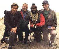 three men are posing for a picture on the beach with one man wearing a hat