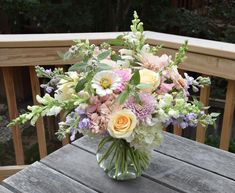 a vase filled with lots of flowers sitting on top of a wooden table next to a railing