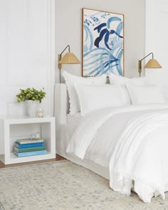 a bed with white sheets and pillows in a bedroom next to a painting on the wall