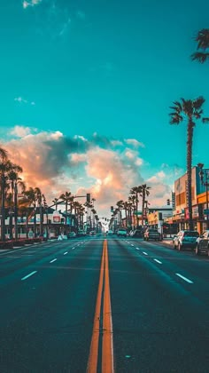 an empty street with palm trees on both sides and the sun setting in the distance