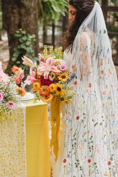 a woman in a wedding dress standing next to a yellow table with flowers on it