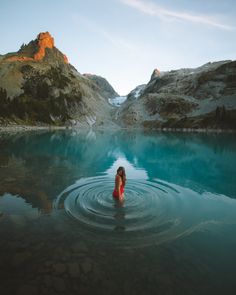 a woman standing in the middle of a lake surrounded by mountains