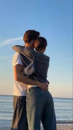 two people standing on the beach hugging each other