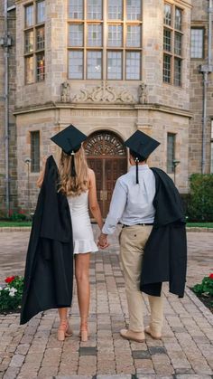 a man and woman in graduation gowns holding hands while walking towards a large building