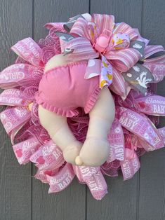 a baby wreath with pink and grey ribbons on the front of a wooden door that says it's a girl