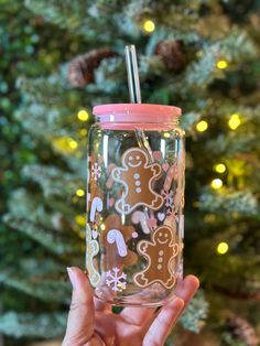 a person holding up a cup with a straw in front of a christmas tree