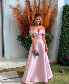 a woman standing in front of a plant wearing a pink dress and holding a purse